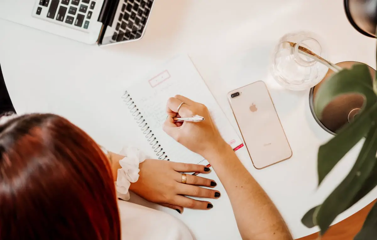 View from above of the woman sitting at the desk writing in the notebook - featured image