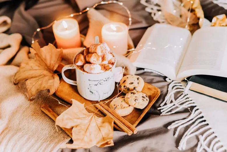 Cup of hot chocolate with marshmallows with a book and lit candles on the side - Liverpool in autumn