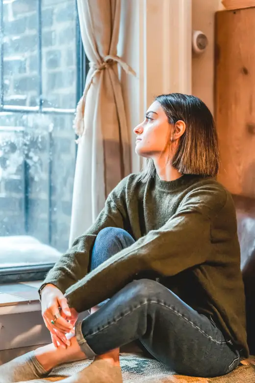 Woman sitting on the bench by the window staring at it mindlessly