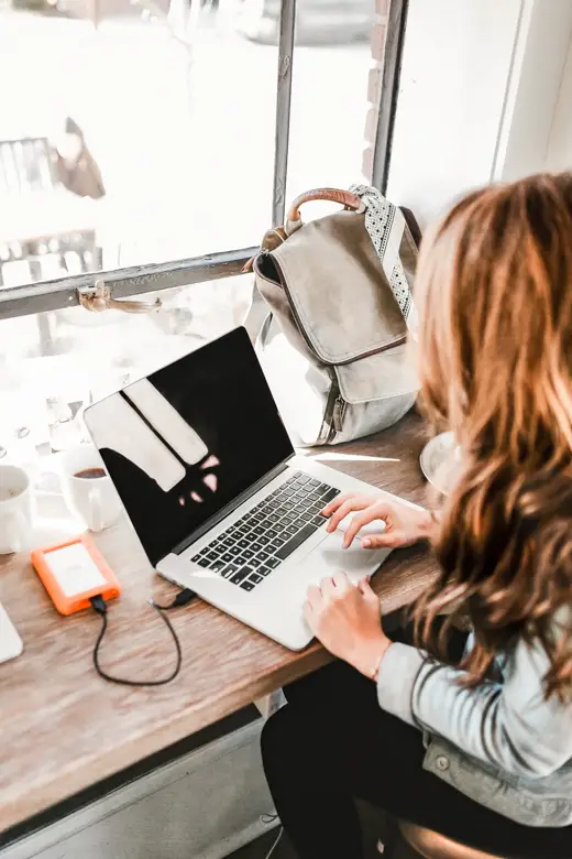 Woman sitting by a wooden table with a laptop, portable drive, and a backpack in front of her - my first blogiversary, 7 things I wish I knew before starting a blog