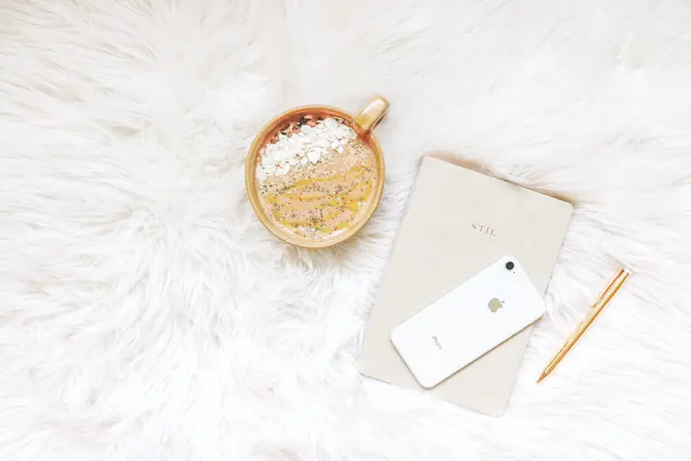 Coffee mug, notebook, pen, and iPhone laying on a white, fluffy blanket - featured image for journaling obstacles