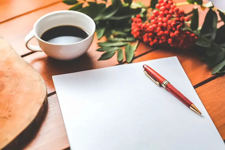 Open loops - piece of paper with red pen, red flowers, and a cup of coffee on wooden desk (featured image)