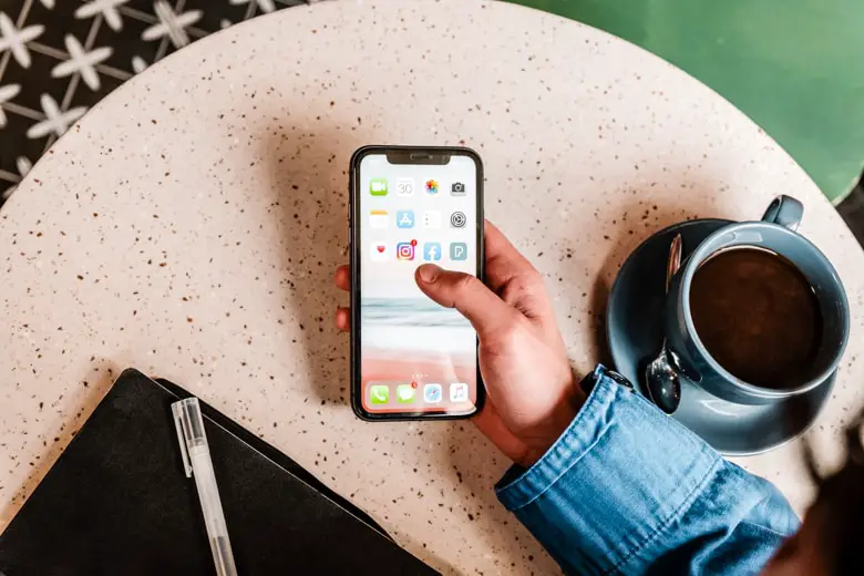 Bird view of a person sitting with a phone by a table and wanting to open social media app - setting social media boundaries