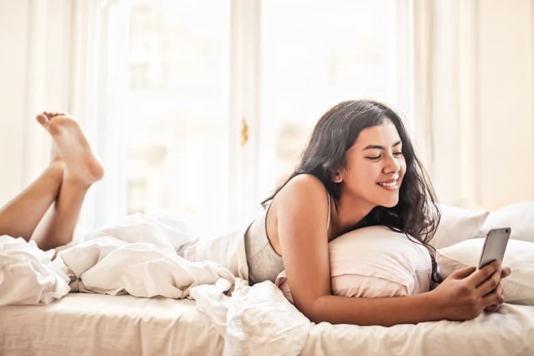 Woman lying on a bed playing on her phone - featured image for setting social media boundaries