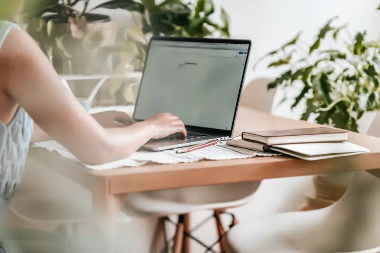 Woman typing on a laptop sitting by a wooden table - featured image for notion and fake productivity