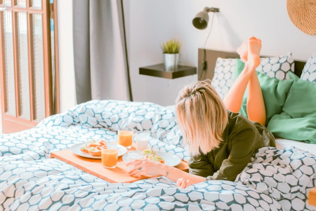woman lying on the bed with breakfast - UK travel apps for finding an accommodation