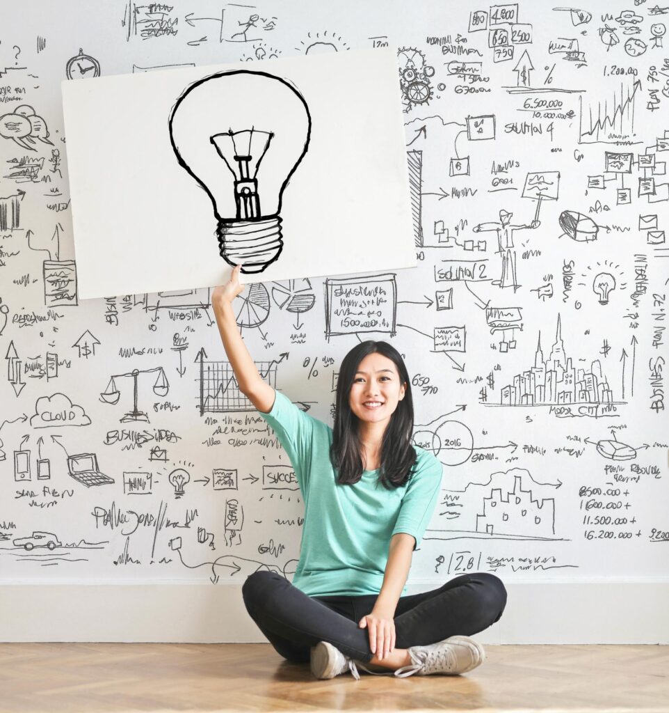 woman sitting on the floor holding a poster with a lightbulb - UK travel apps for getting inspired