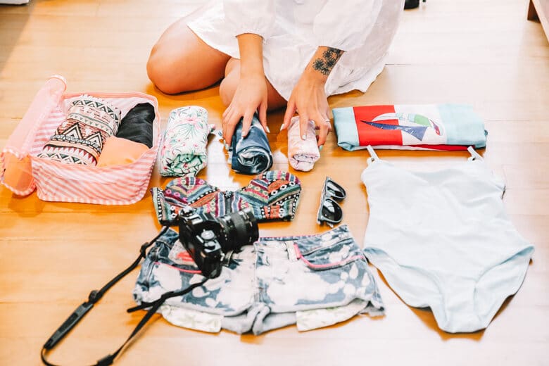 Woman rolling up clothes, sitting in front of her belongings ready to pack