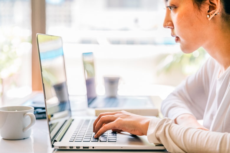 Woman in a white blouse sits in front of the laptop with a mug behind it - blogging advantages and disadvantages
