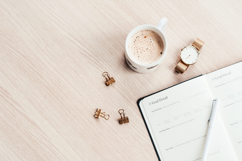 Bird view of white cup of coffee, gold watch, a notebook and some pieces of stationery laying on the wodden table - featured image for what to do when your plan fails