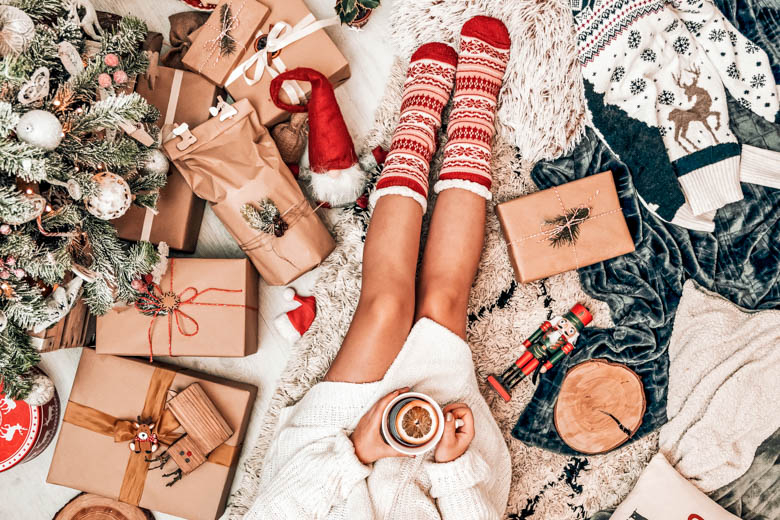 Bird view of a women sitting on a floor with a cup of coffee surounded by wrapped presents and Christmas ornaments - 12 days of Christmas self care
