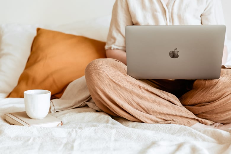 Woman sitting with her Macbook on a bed with a cup of cofee on the side - featured image for December 2022 blog growth report