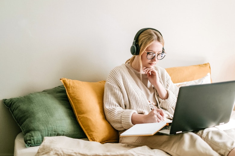 Blonde woman sitting on a bed with a notebook and a laptop - featured image for monthly reset routine