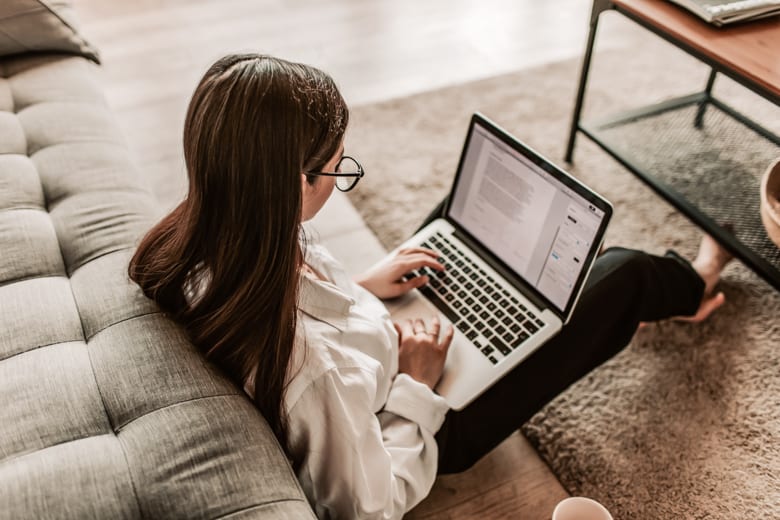Woman sitting on a floor and typing on a keyboard - featured image for how to write blog posts faster